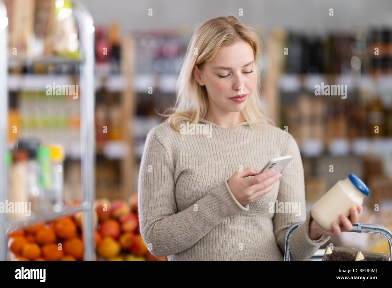 L'acquirente donna verifica l'idoneità - scansiona il codice QR sul barattolo dell'etichetta maionese nel negozio di alimentari Foto Stock