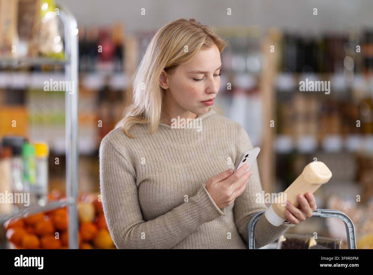 L'acquirente donna verifica l'idoneità - scansiona il codice QR sul barattolo dell'etichetta maionese nel negozio di alimentari Foto Stock