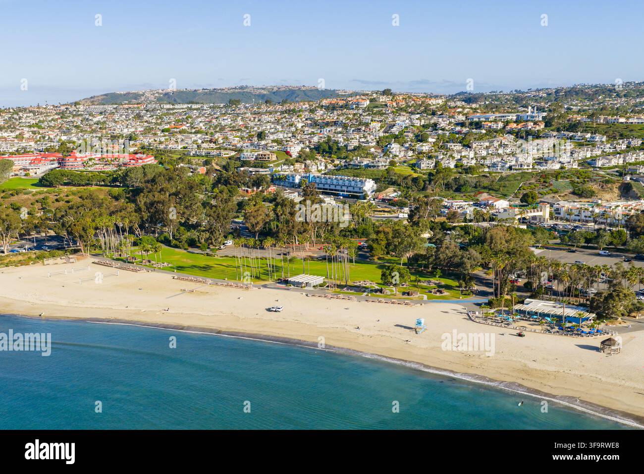 Vista aerea della spiaggia di Dana Point con una battigia sabbiosa, un parco verde, palme e case sui pendii che si affacciano sull'Oceano Pacifico a Dana P Foto Stock