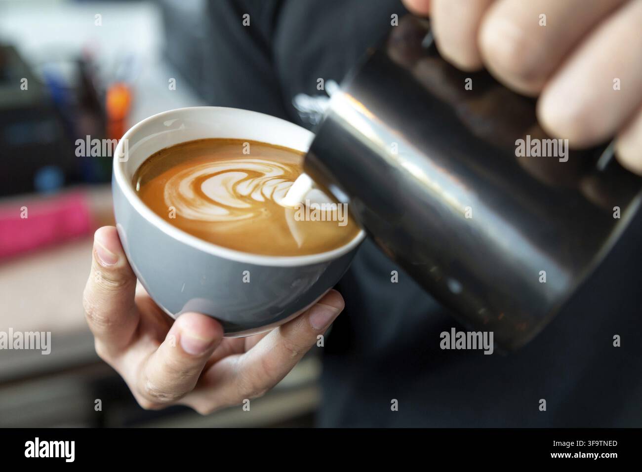 Barista che prepara il caffè latte, versando il latte in un caffè. Primo piano sulle mani maschili con latte art. Foto Stock