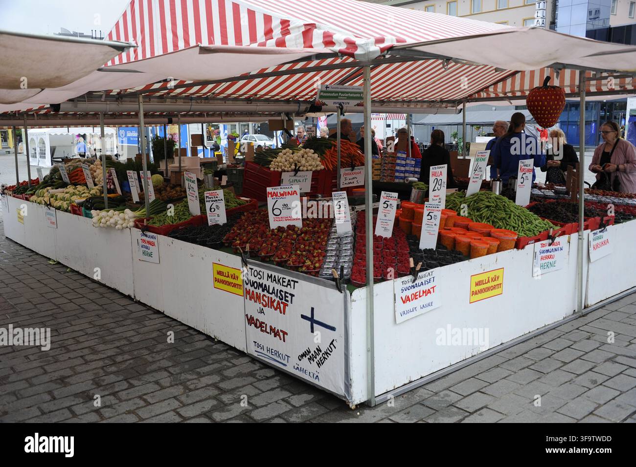 Un vivace banco di mercato a Savonlinna, Finlandia, pieno di bacche locali fresche, fragole, piselli e verdure sotto una tenda a strisce. Foto Stock