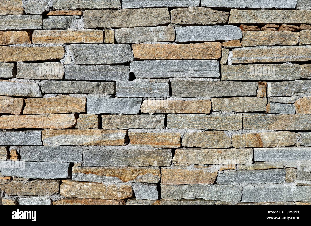 Muro realizzato con strisce di pietra di luserna con colori che vanno dal grigio blu al marrone e al giallo dorato. Rivestimento rustico per esterni. Texture Foto Stock