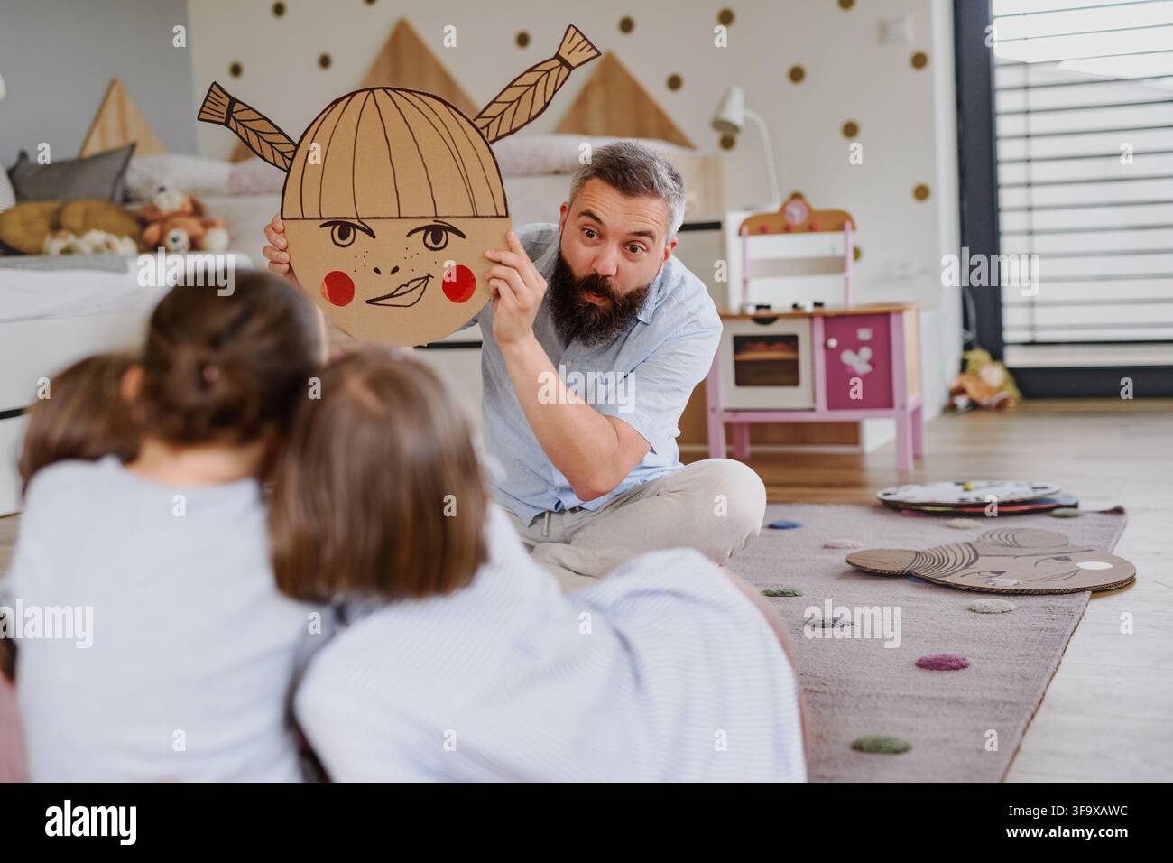 Padre che insegna alle figlie le emozioni utilizzando espressioni facciali illustrate a casa. Foto Stock
