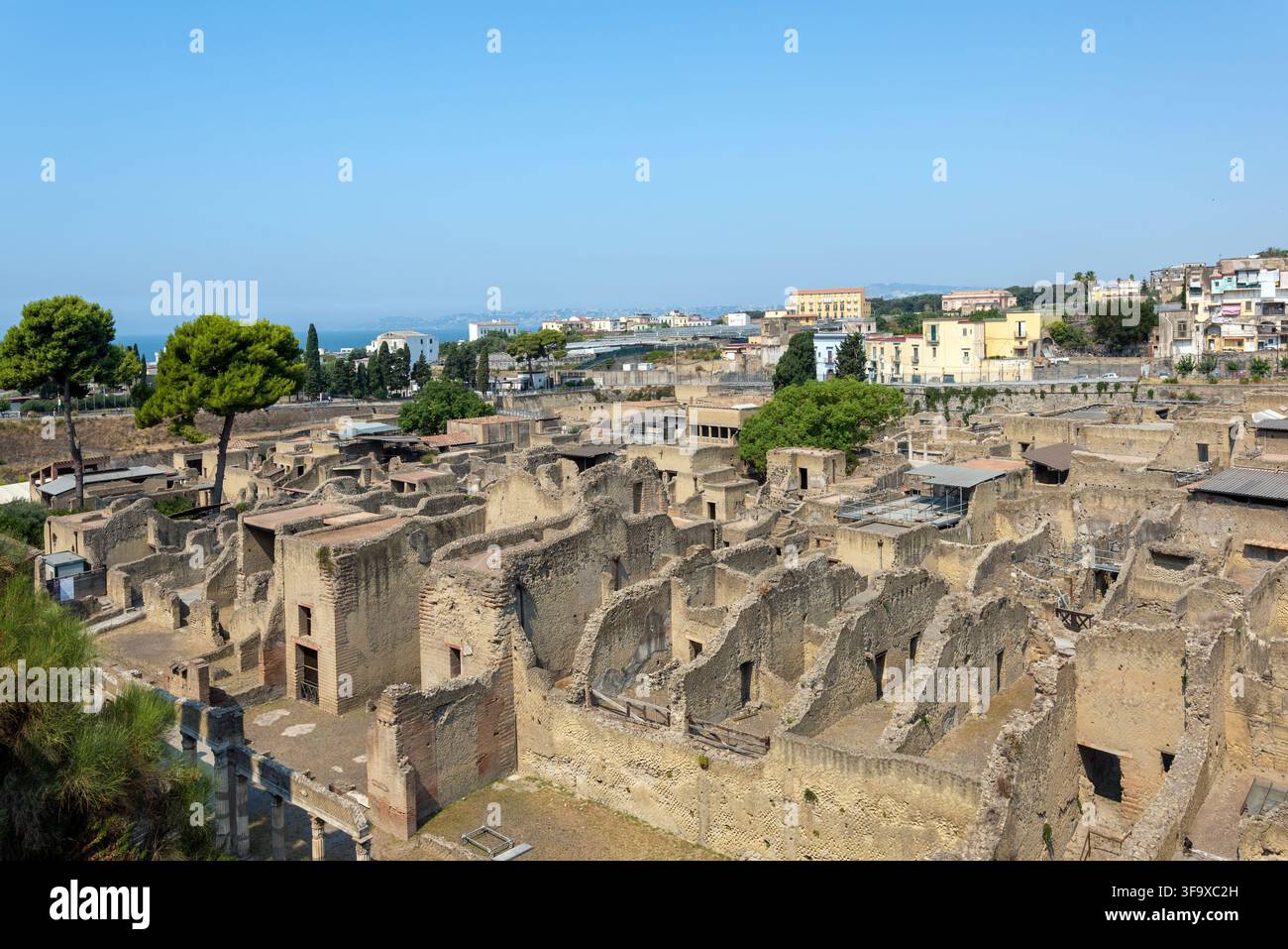 Vista panoramica sull'antica città romana verso la baia di Napoli, con pini a ombrello e edifici moderni nel Parco Archeologico di Ercolano Foto Stock