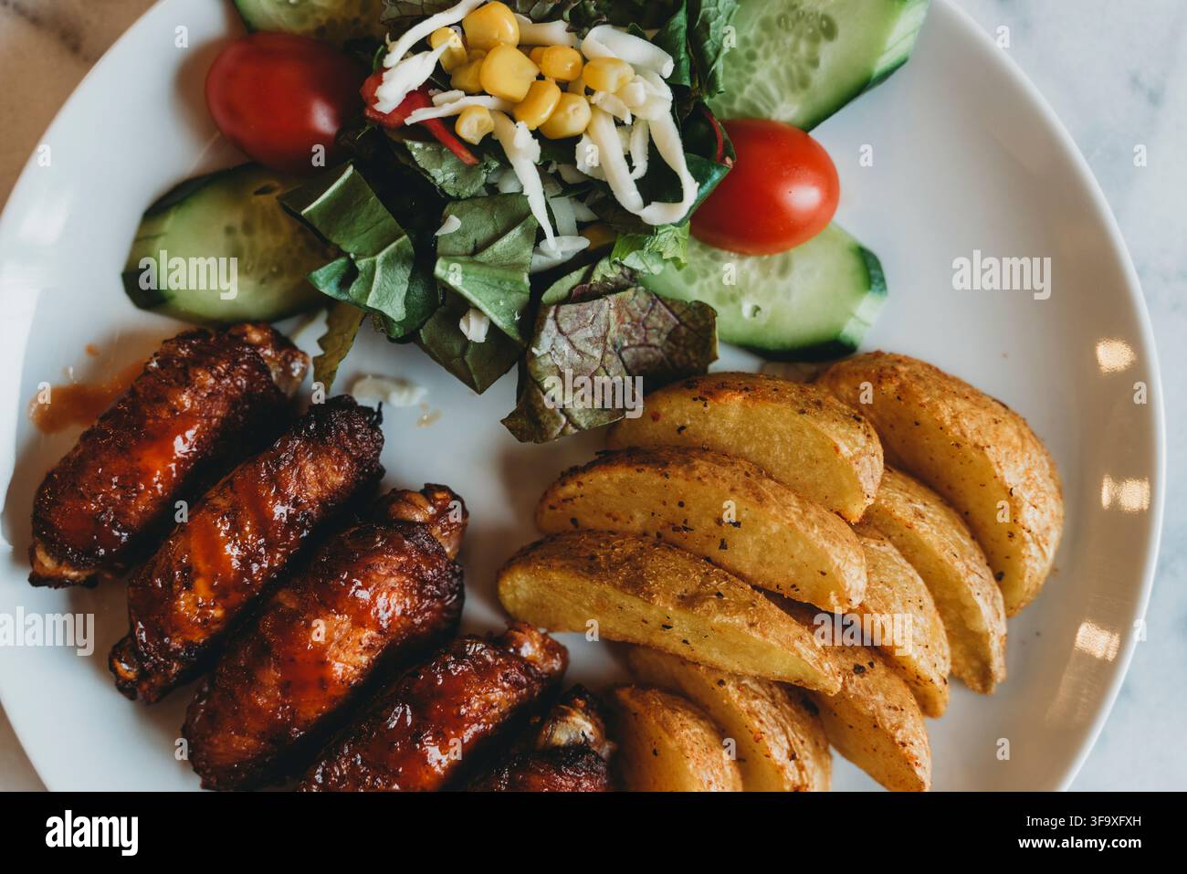 Alette di pollo al barbecue con patate a cubetti e insalata Foto Stock