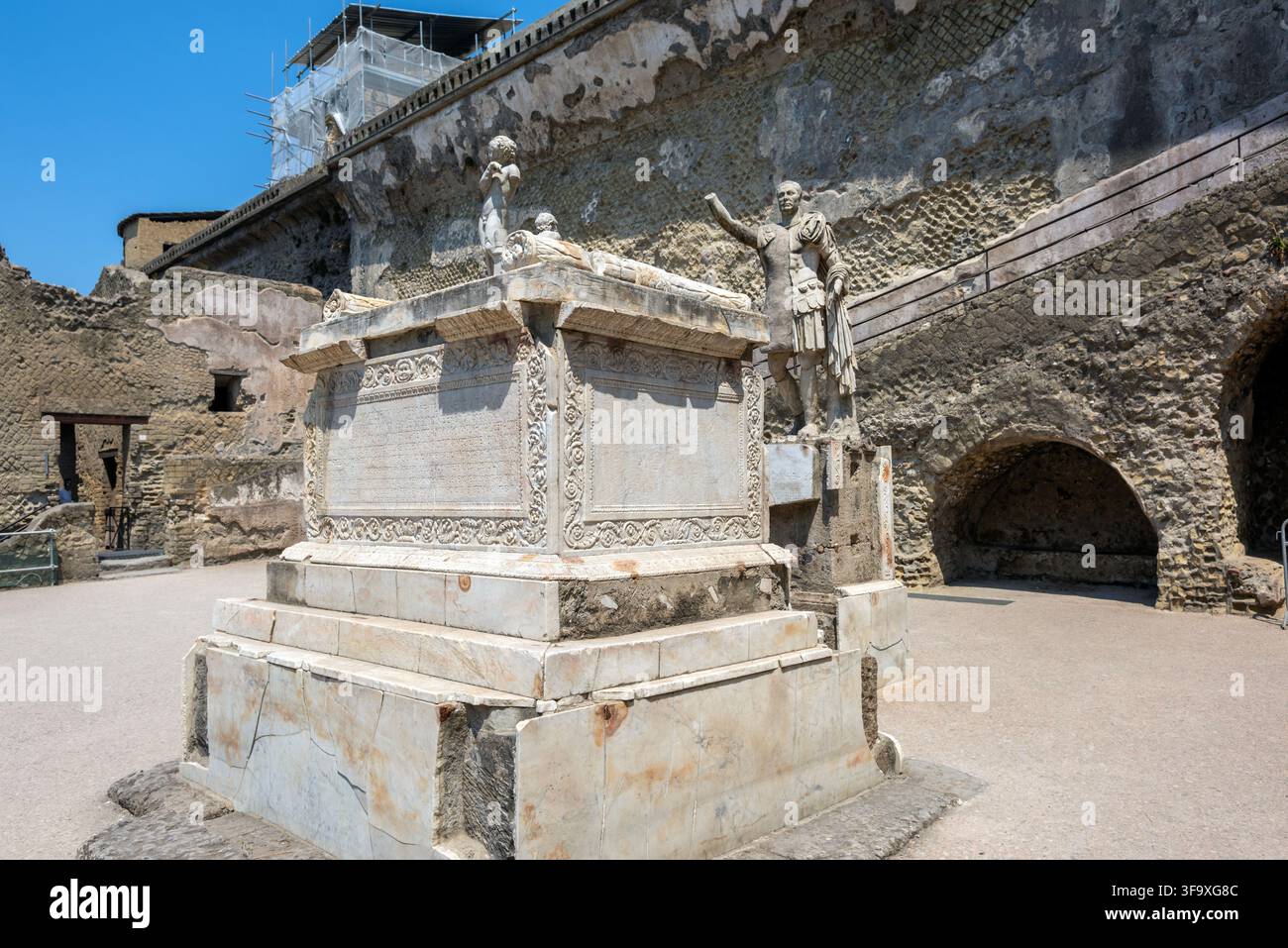 Ampia vista a tre quarti del monumento funebre in marmo e della statua di Marcus Nonius Balbus nel Parco Archeologico di Ercolano, Italia. Foto Stock