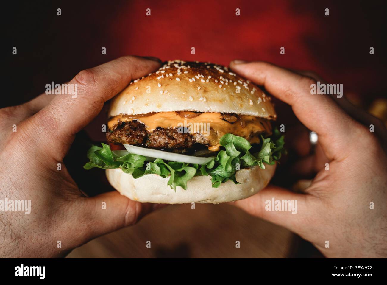 Mani che tengono un grande cheeseburger succoso Foto Stock
