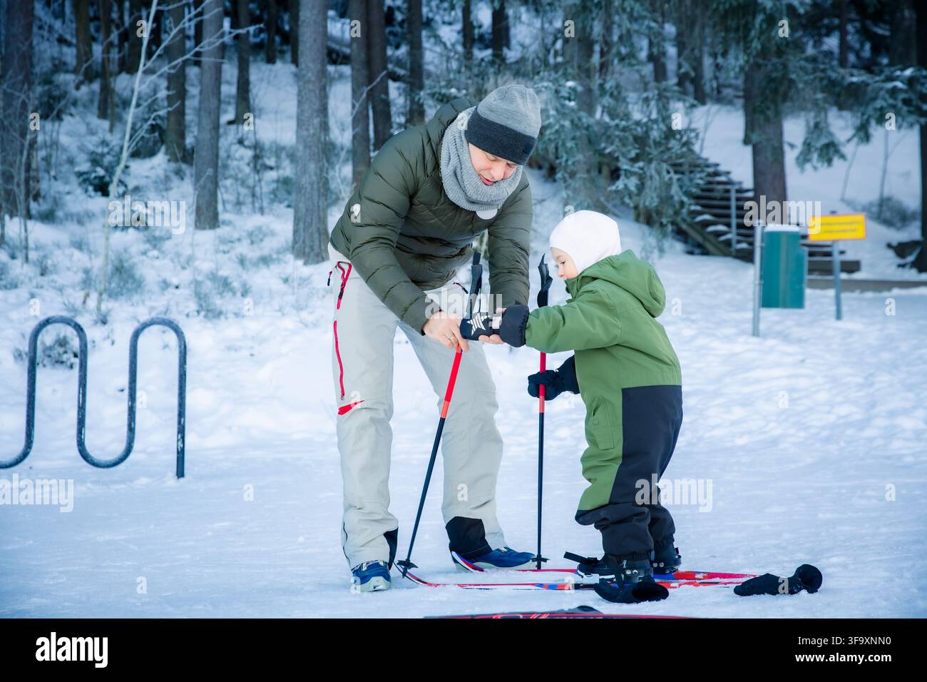 Padre che aiuta il figlio con gli sci nella foresta finlandese. Attiva vacanza invernale in famiglia, Scandinavia. Stile di vita nordico, genitorialità, sport all'aperto. Persone vere. Foto Stock