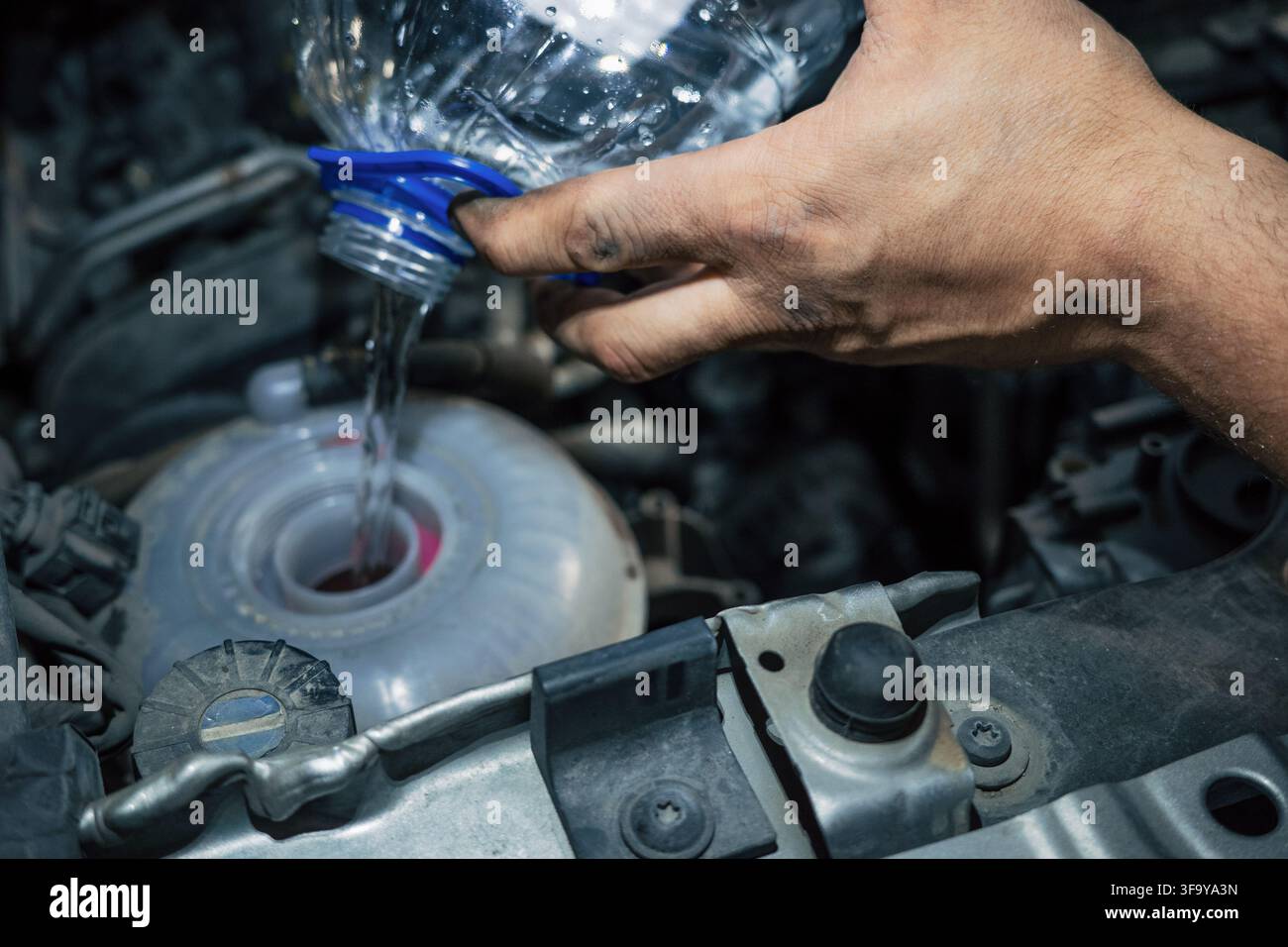 Meccanico che versa antigelo nel serbatoio del liquido refrigerante durante la revisione, riparazione e manutenzione del motore. Foto Stock