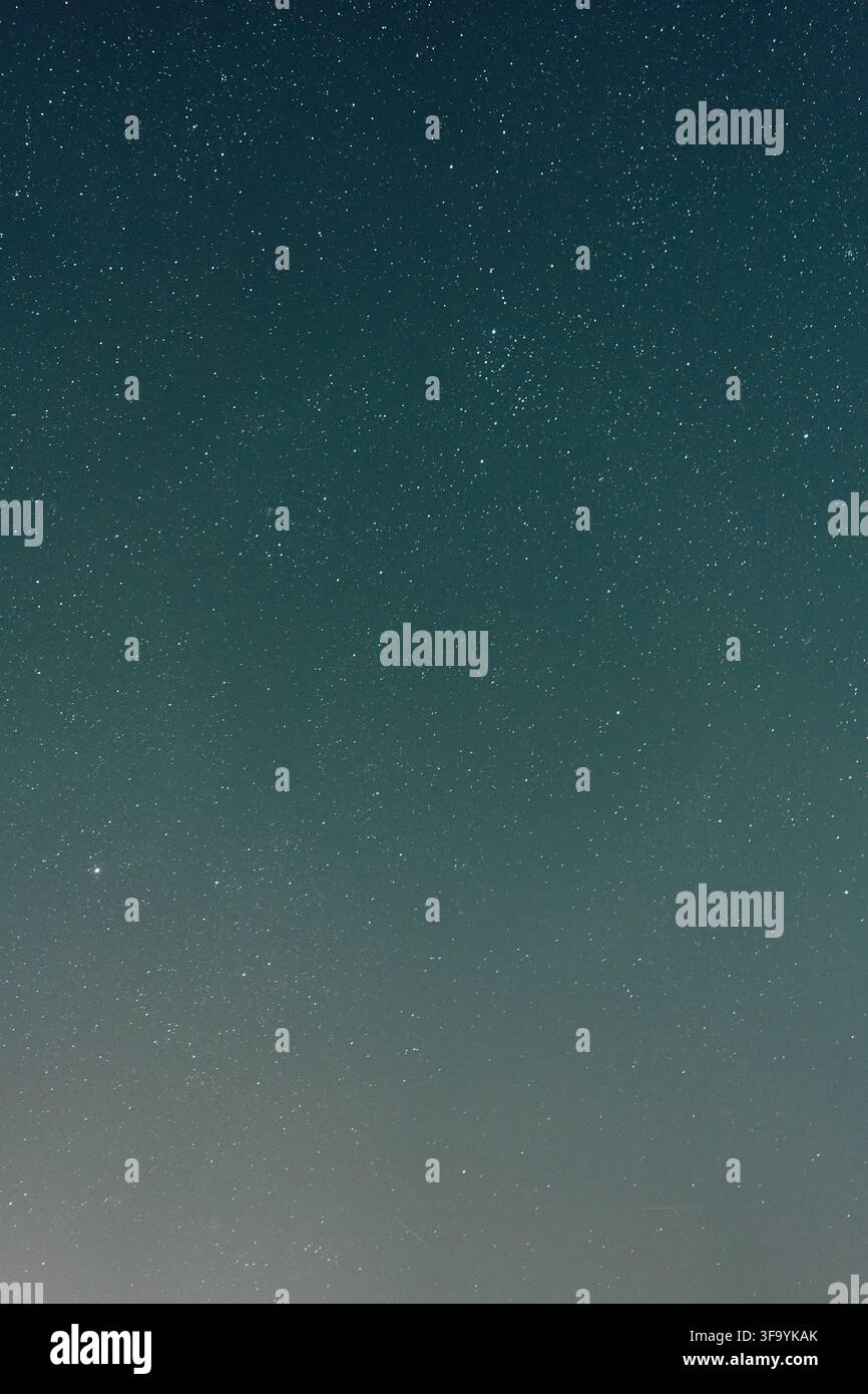 Cielo notturno stellato sopra un orizzonte debolmente luminoso con sfumatura blu-verde, punti di luce bianchi sparsi, atmosfera scura e calma, luce minima Foto Stock