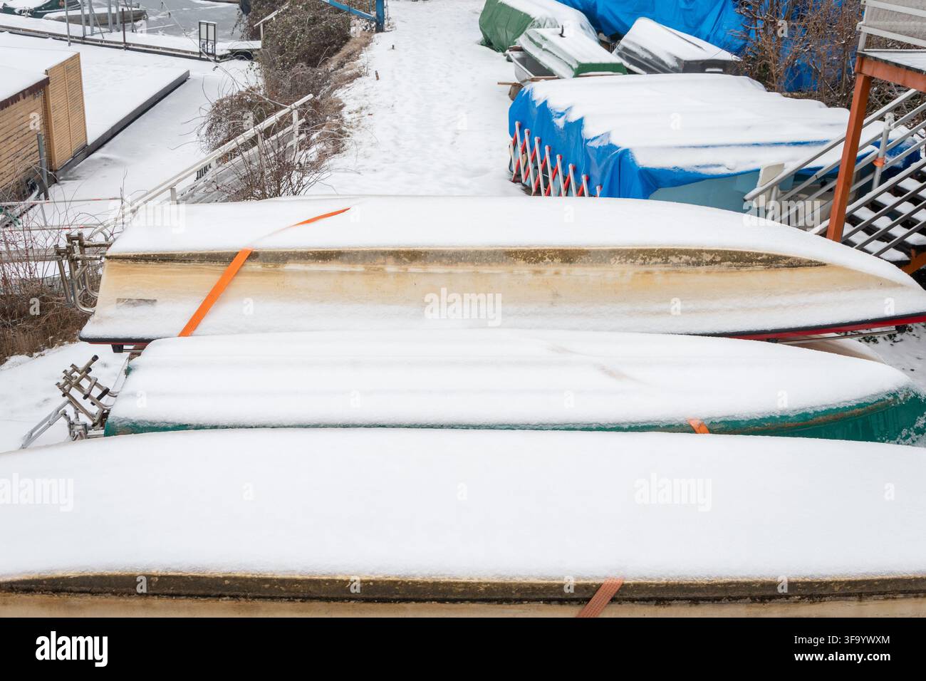 Diverse barche capovolte sono coperte di neve in un'area di stoccaggio all'aperto durante l'inverno. Foto Stock
