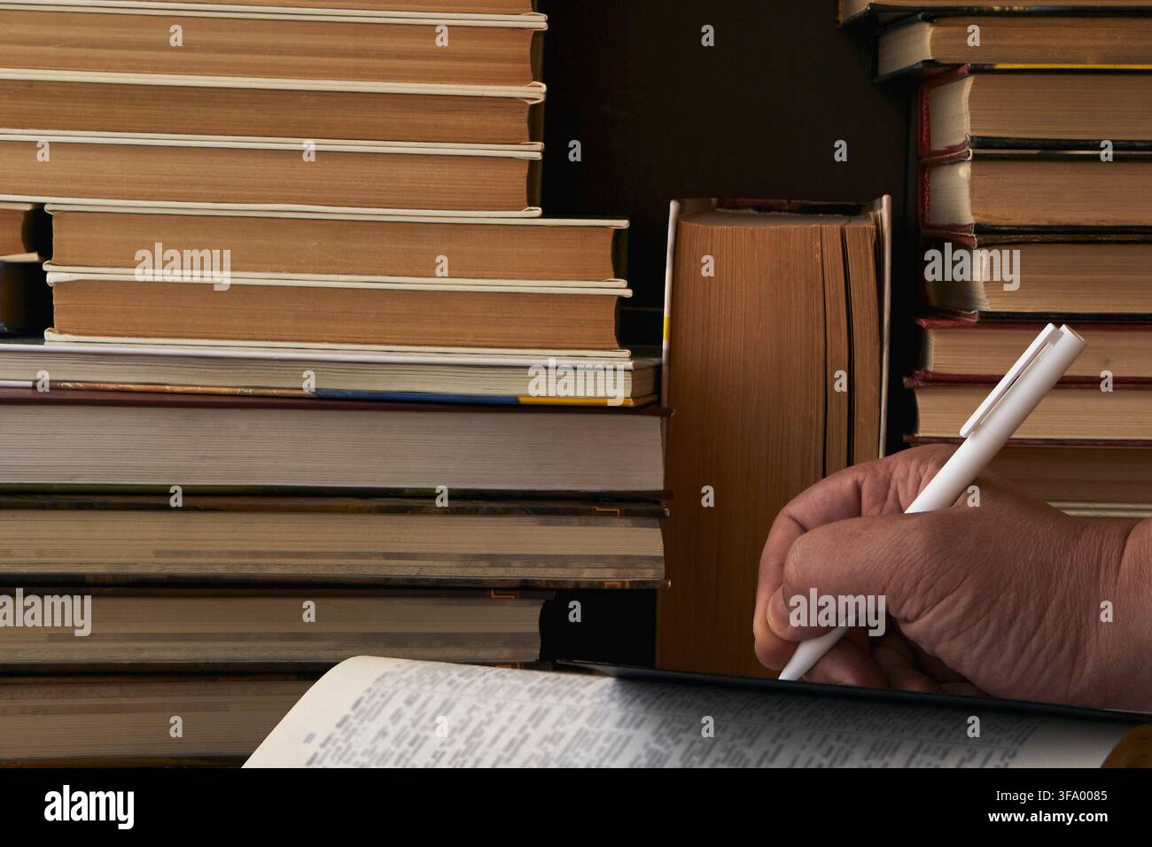 Una mano con una penna scrive in un taccuino tra i libri. Foto Stock