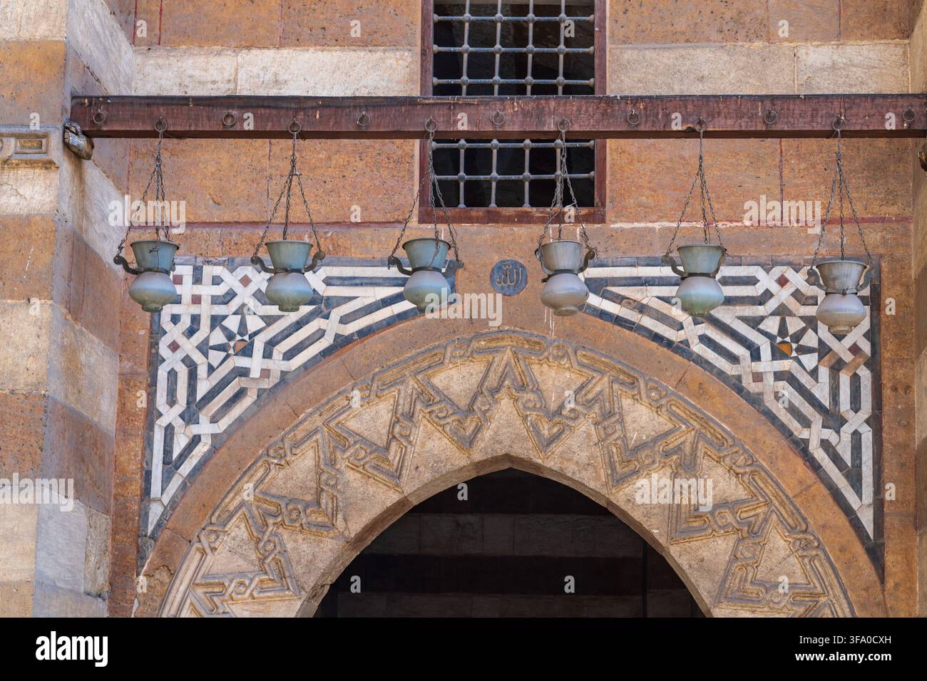 Vista dell'ingresso in pietra intricato e dei motivi geometrici del complesso funerario di Amir Khayrbak con lampade metalliche sospese a El-Darb El-Ahmar, Il Cairo Foto Stock