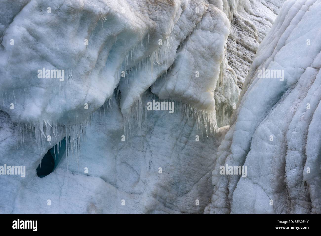 Formazioni di ghiaccio glaciale che mostrano superfici texture, un'apertura di una grotta di ghiaccio blu profondo e numerose gocce di ghiaccio che creano un paesaggio artico congelato e astratto Foto Stock