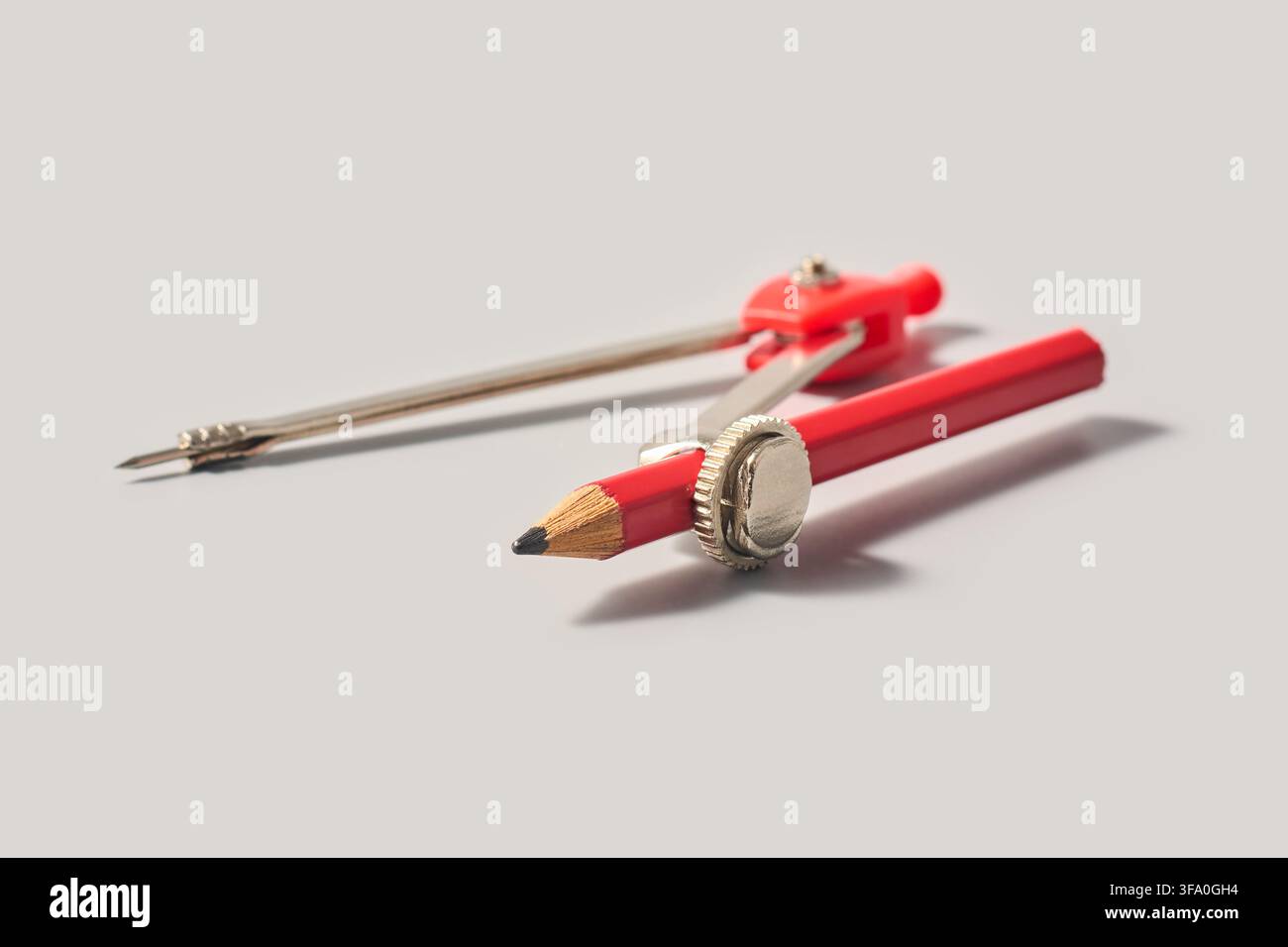 compasso geometrico rosso con matita su sfondo grigio isolato, strumento da disegno in metallo e plastica con punta affilata in messa a fuoco morbida, primo piano vista laterale Foto Stock