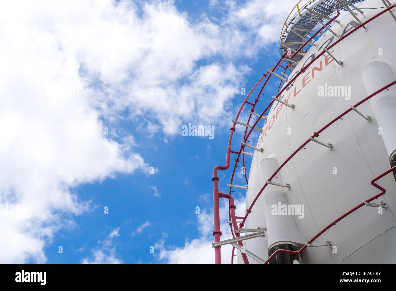 Vista ad angolo basso di un grande serbatoio sferico bianco di propilene con tubazioni rosse e scala su un cielo blu con nuvole bianche in un'installazione petrolchimica Foto Stock