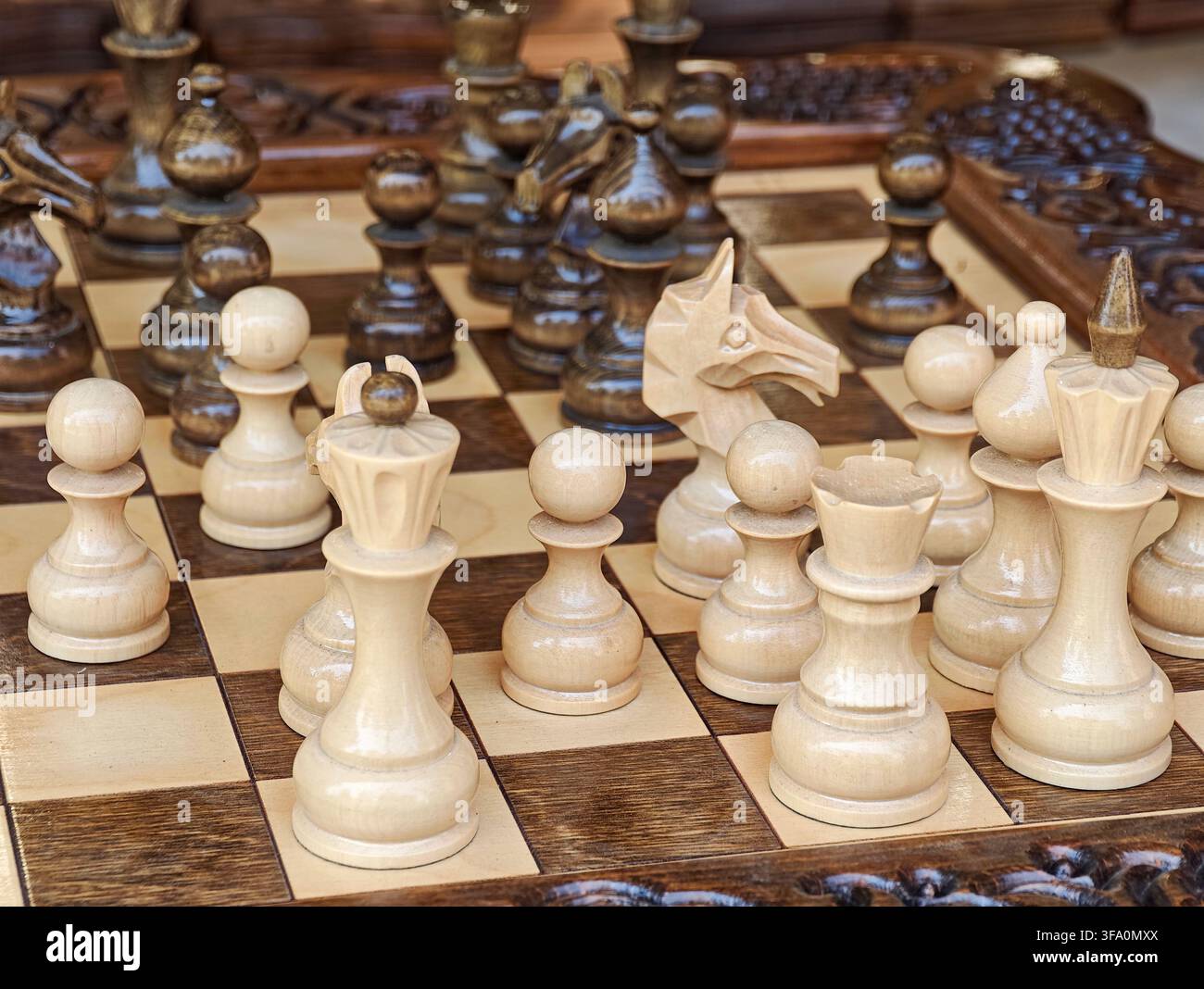 Set di scacchi con pezzi in legno intagliati su scacchiera a quadretti. I pezzi includono re, regina, torre, alfiere, cavaliere e pedina. La scacchiera ha quadrati di legno scuro e chiaro Foto Stock