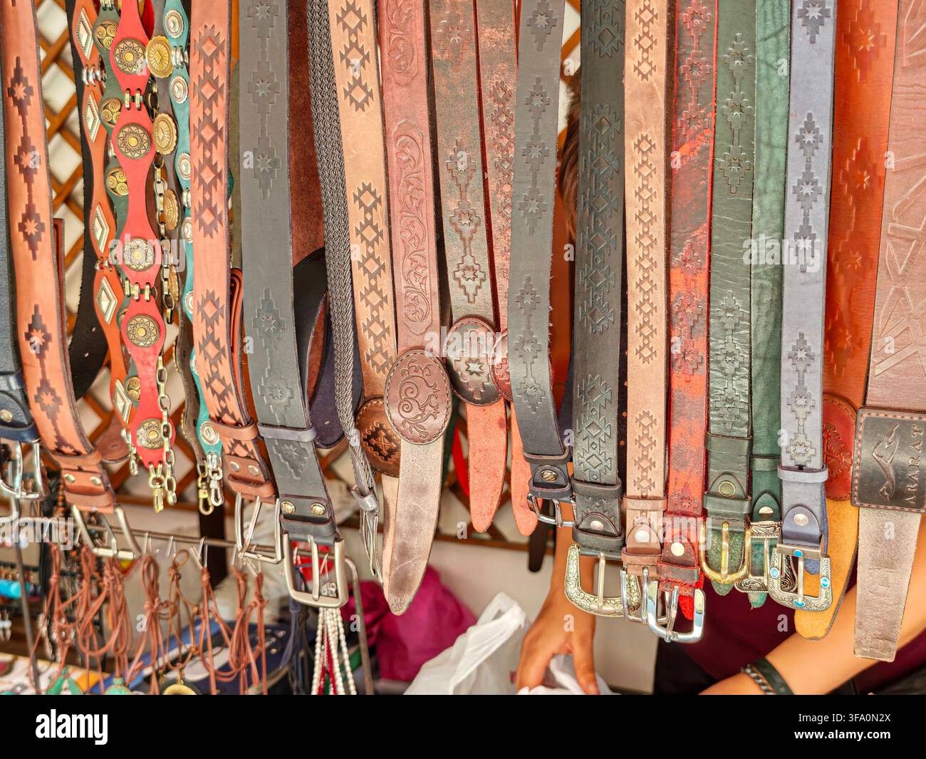 Collezione di cinture appesa in negozio. Diversi design e colori esposti. Fibbie in metallo e motivi decorativi visibili. Articoli disposti verticalmente per e Foto Stock