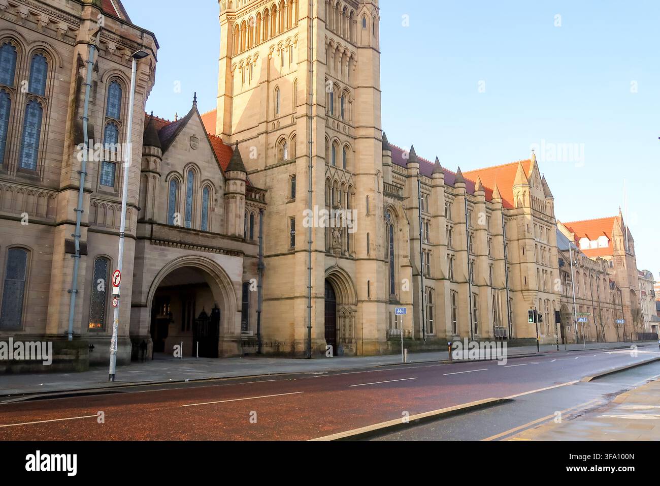 Vista illuminata dal sole degli edifici gotici storici dell'Università di Manchester lungo Oxford Road a Manchester, Inghilterra, con facciate in pietra ornate, torri, arcate Foto Stock