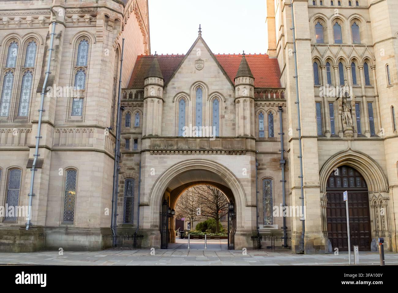 Arco gotico storico e facciata in pietra ornata all'Università di Manchester, Inghilterra, che mostra l'architettura accademica vittoriana e un campus tranquillo Foto Stock