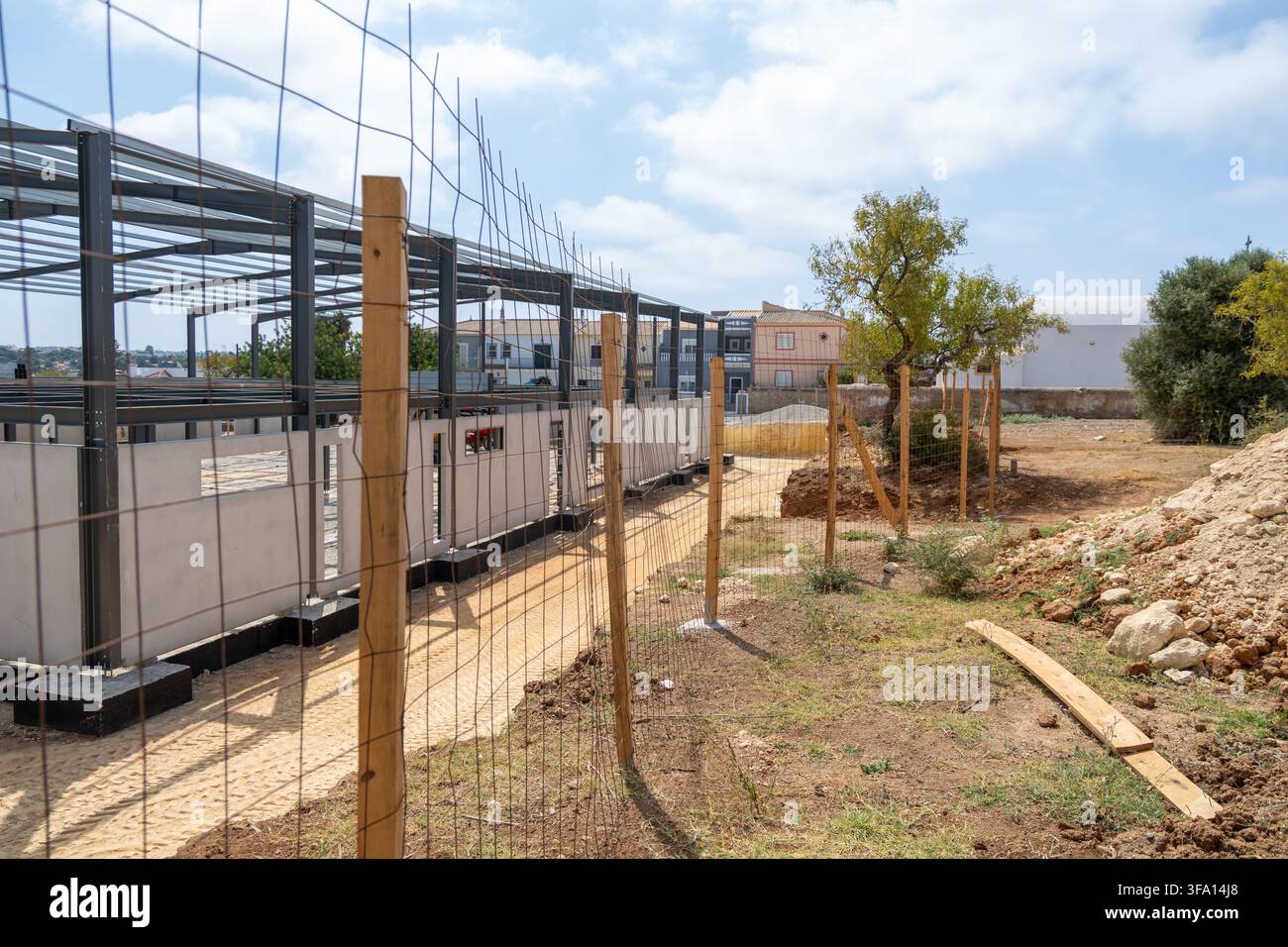 Una nuova struttura in acciaio viene eretta in un cantiere con pannelli murari in cemento e recinzioni temporanee che circondano l'area Foto Stock