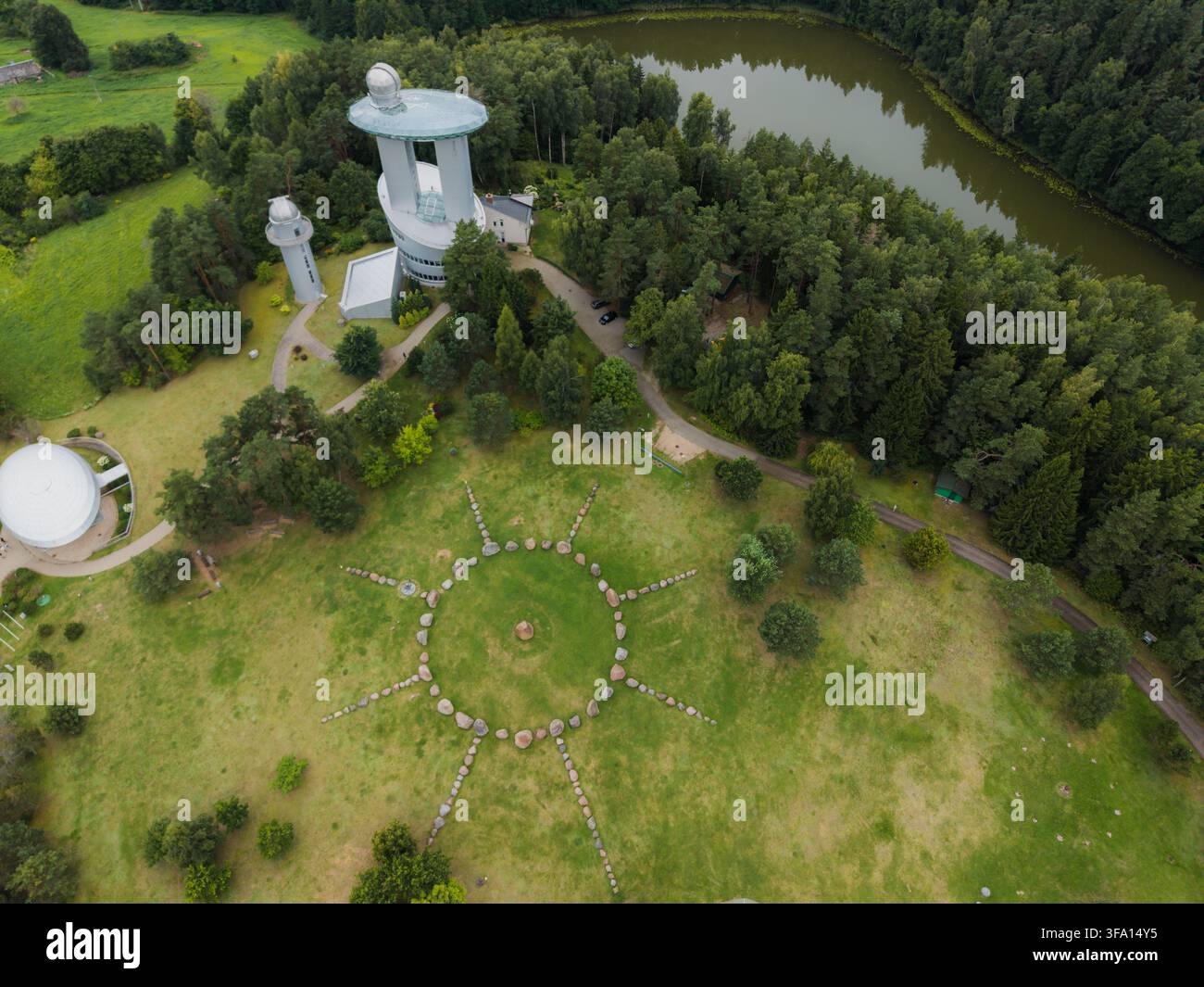 Vista aerea del Museo Lituanico di Etnocosmologia, con torri osservatori, un simbolo solare in pietra sull'erba, foresta e un lago vicino a Ku Foto Stock