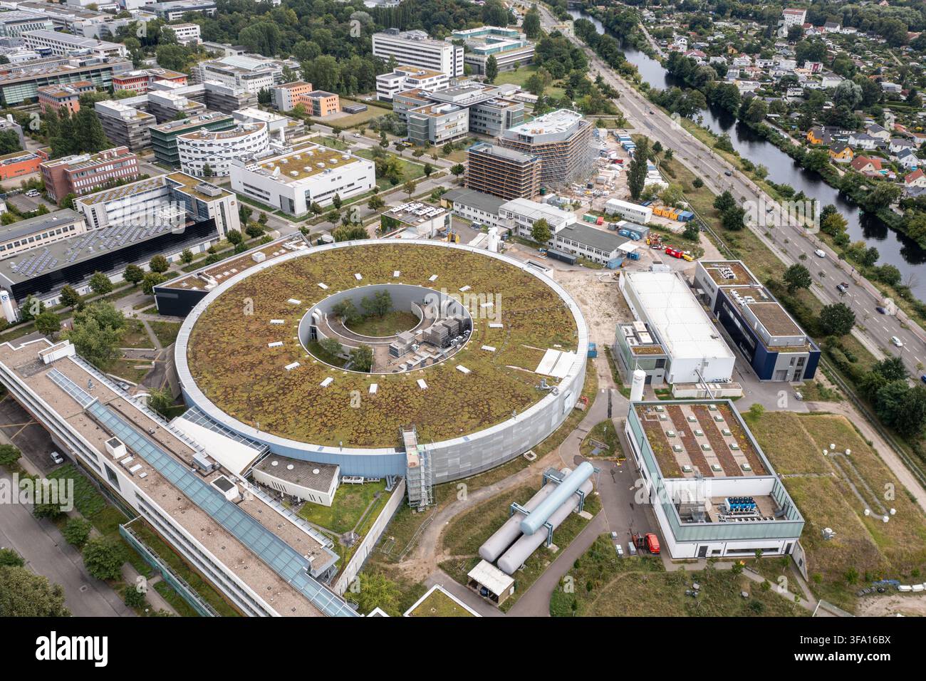 Vista aerea dell'edificio circolare del sincrotrone BESSY II con tetto verde presso l'Helmholtz-Zentrum Berlin, circondato da strutture di ricerca e verde Foto Stock