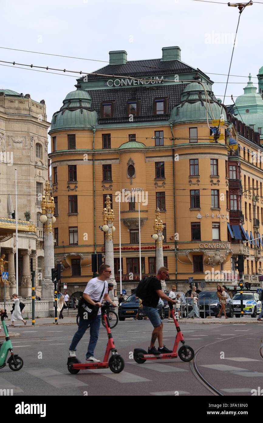 Tre scooter elettrici a noleggio che attraversano un passaggio pedonale a Stoccolma con il Teatro Drammatico Reale sullo sfondo. Foto Stock