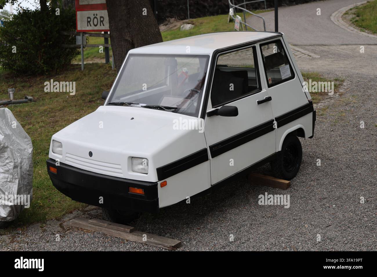 Un piccolo motorino bianco a tre ruote di classe II parcheggiato sulla ghiaia accanto al lungomare in una giornata estiva soleggiata a Stoccolma, Svezia. Foto Stock