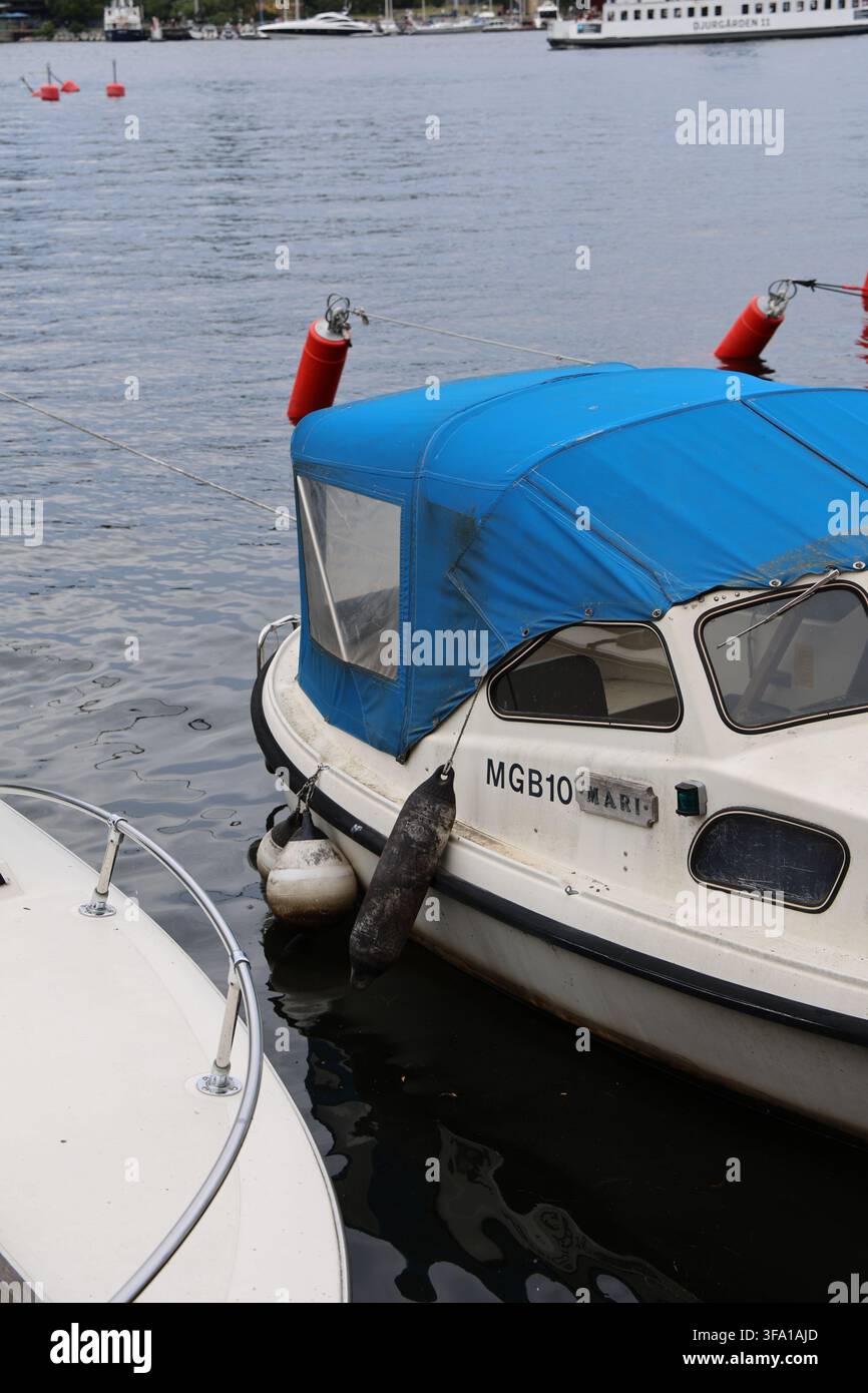 Piccole barche ormeggiate lungo il molo di Skeppsholmen a Stoccolma, Svezia, con il lungomare e le acque calme nelle vicinanze. Foto Stock