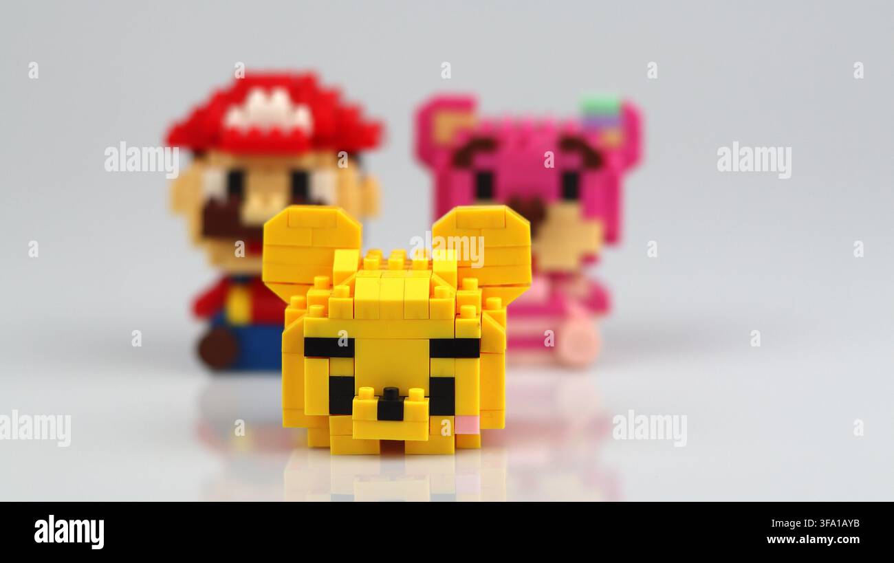Figura a blocco di orso giallo in primo piano con Mario e un personaggio giocattolo rosa leggermente sfocato sullo sfondo. Foto Stock