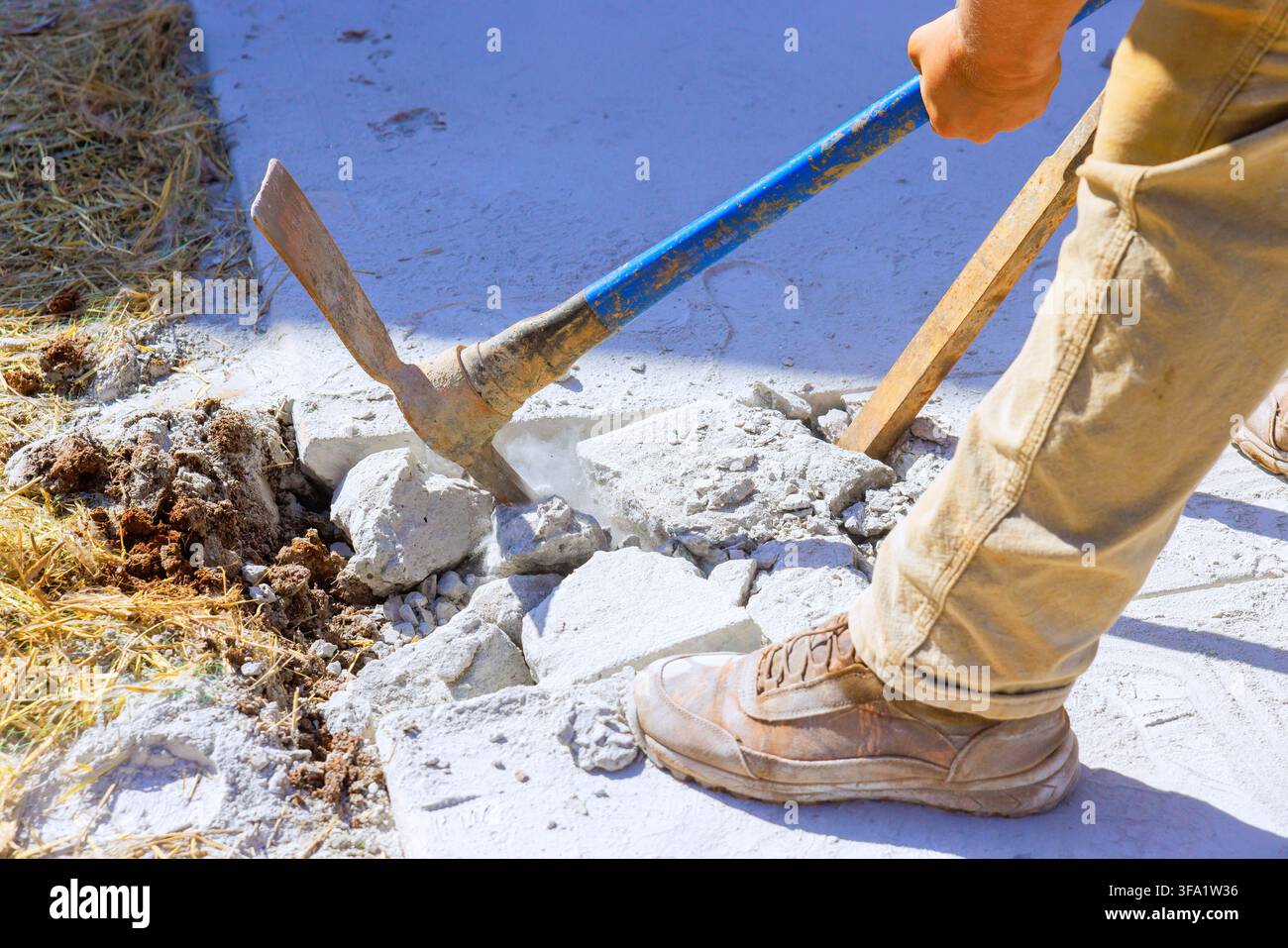 Lavoratore rompe una lastra di cemento con un piccone in acciaio nel cantiere Foto Stock