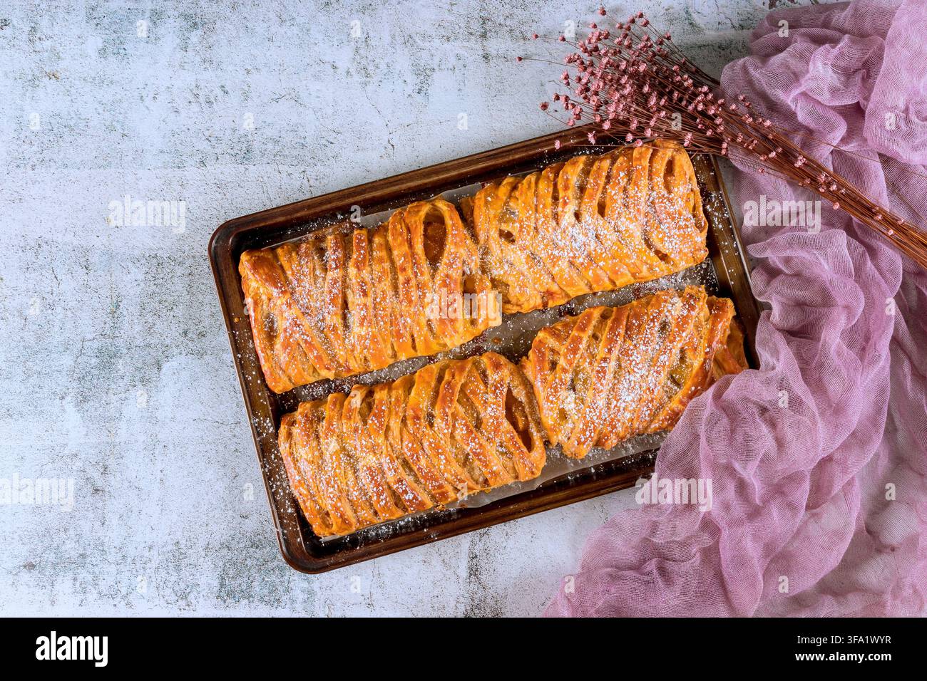 Pasticceria posata su un vassoio spolverato di zucchero a velo posizionato vicino a una scena di tessuto lavanda mostra un allestimento da panetteria. Foto Stock