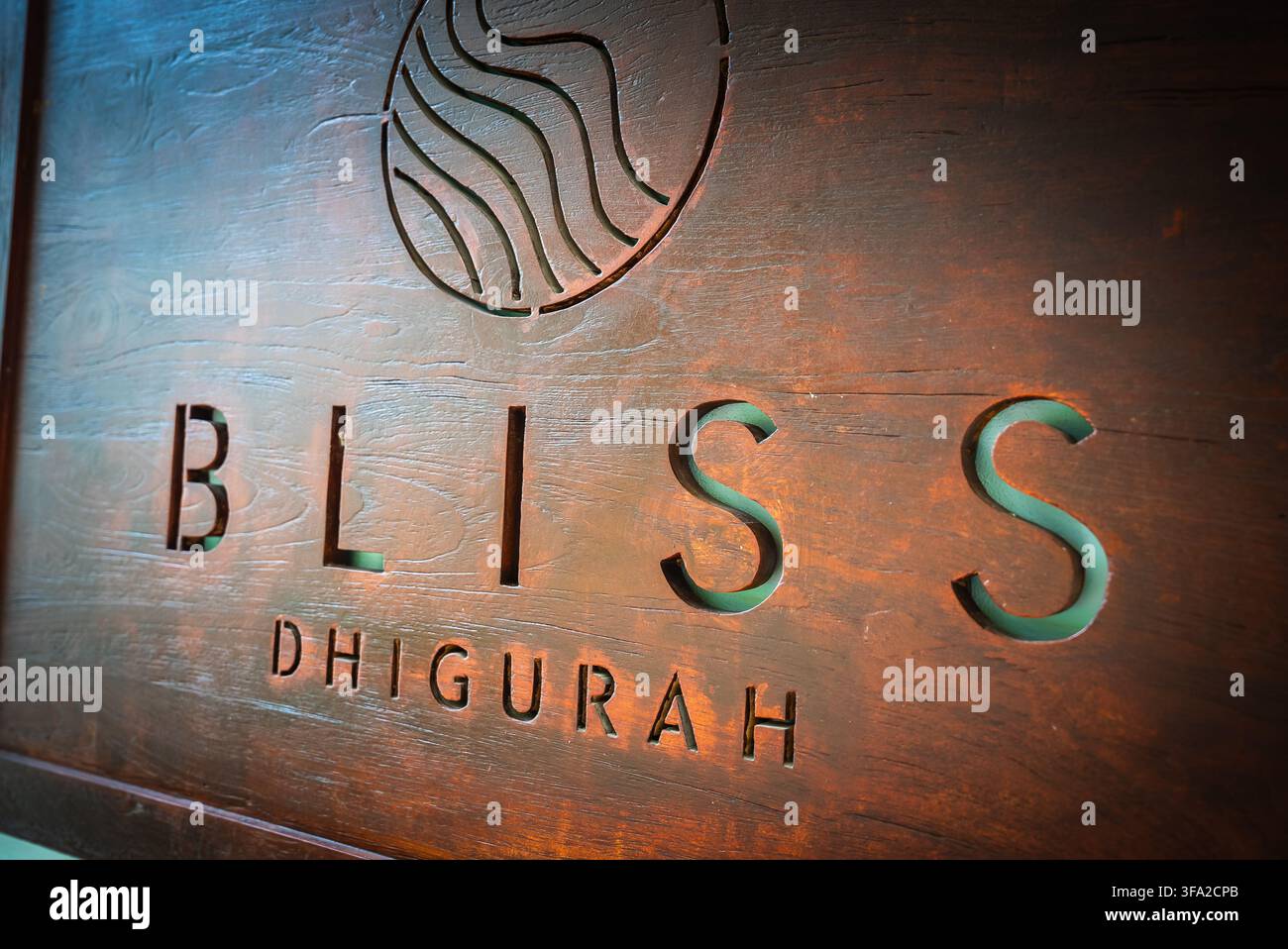 Un primo piano di una targa di legno incisa con la scritta Bliss Dhigurah e un logo a forma di onda circolare intagliato in un pannello di legno scuro. Foto Stock