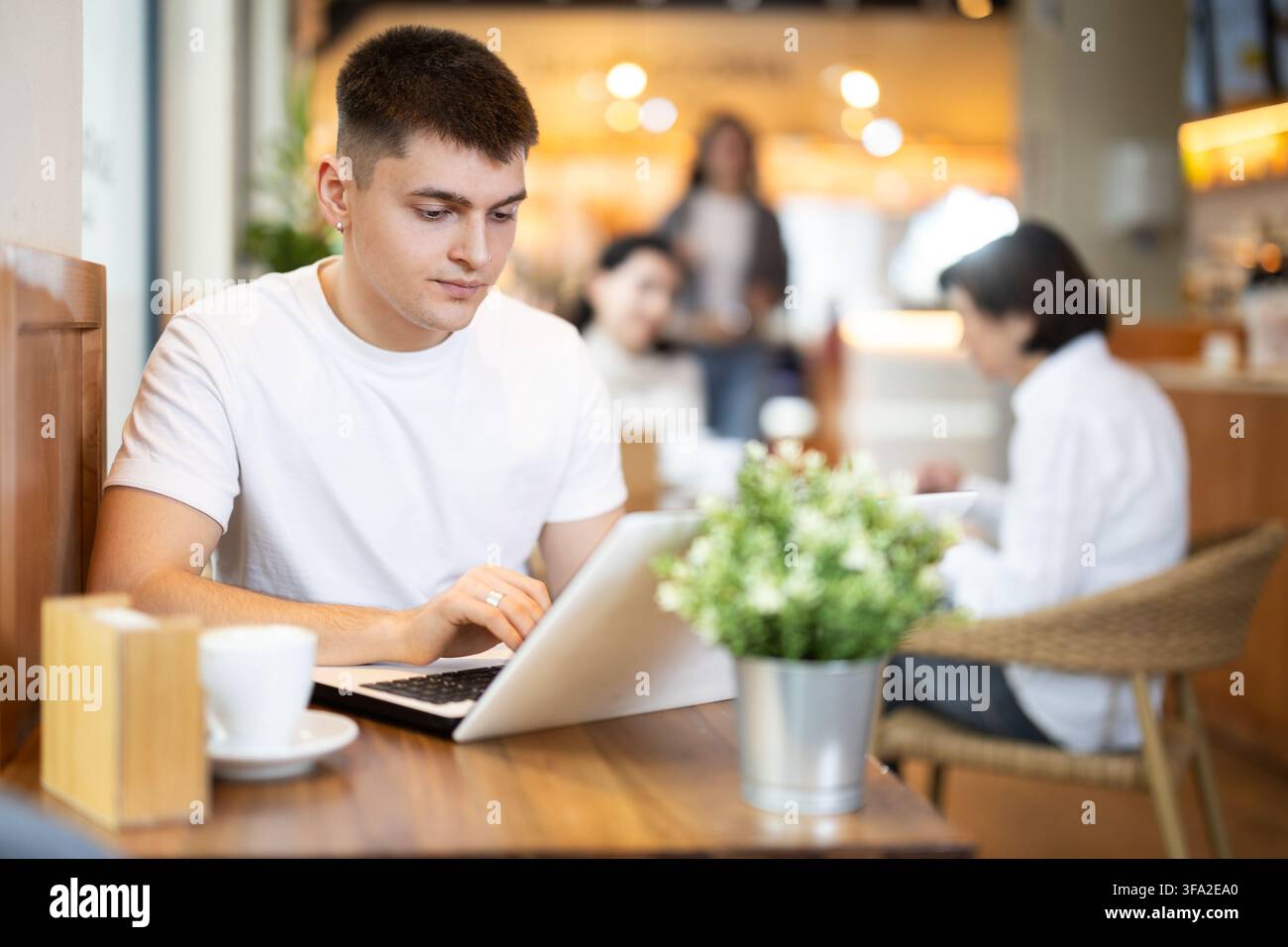 Giovane seduto in un bar e che lavora con un computer portatile Foto Stock