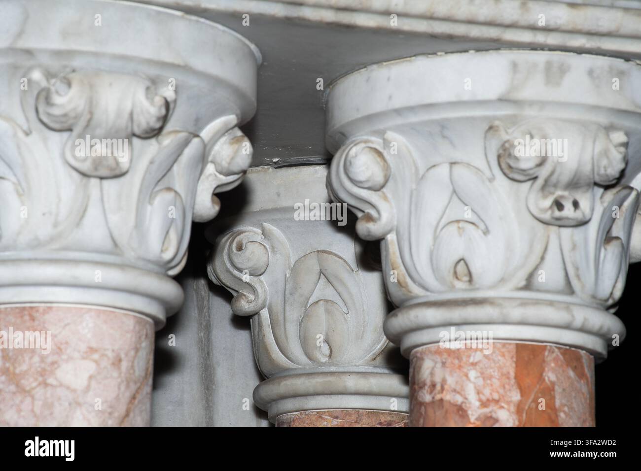 Primo piano di capitelli di colonne in marmo ornati con foglie d'acanto e intagli a volute sopra fusti di marmo venato di rosa all'interno di un mausoleo. Foto Stock