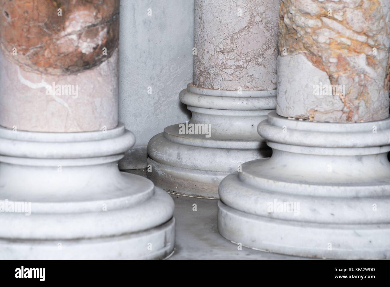 Primo piano di tre basi di colonne in marmo che mostrano una pietra rosa sorprendente con venature ruggine su marmo grigio pallido, all'interno di un mausoleo scarsamente illuminato. Foto Stock