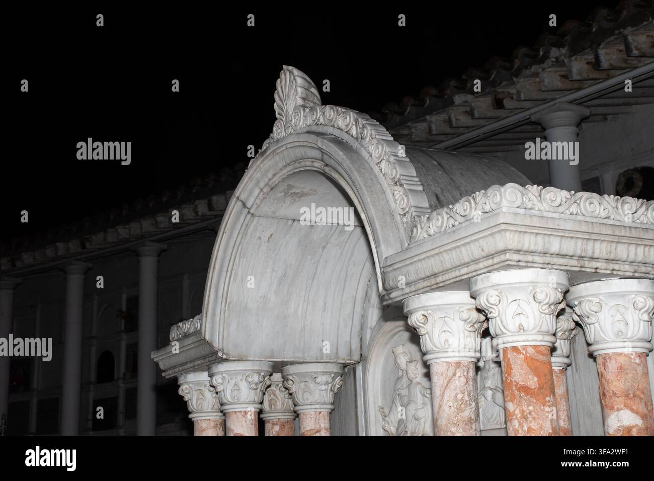Vista notturna drammatica della linea del tetto di un mausoleo in marmo ornato con cornice a volute e capitelli corinzi sopra colonne di marmo con venature rosa, illuminato contro Foto Stock