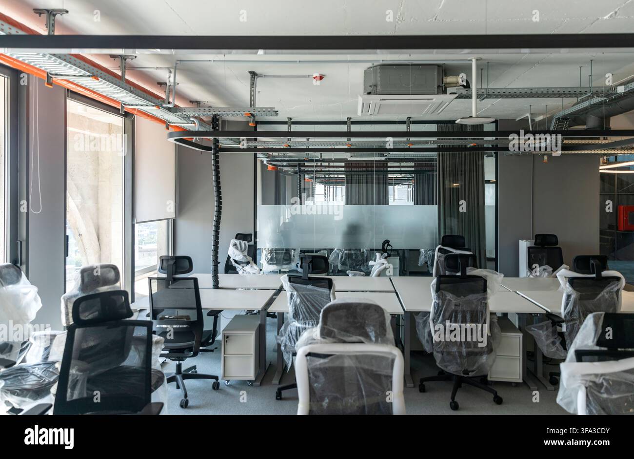 Ufficio open-space vuoto dotato di nuove scrivanie, sedie avvolte nella plastica e vassoi per cavi a vista sul soffitto prima dell'apertura Foto Stock