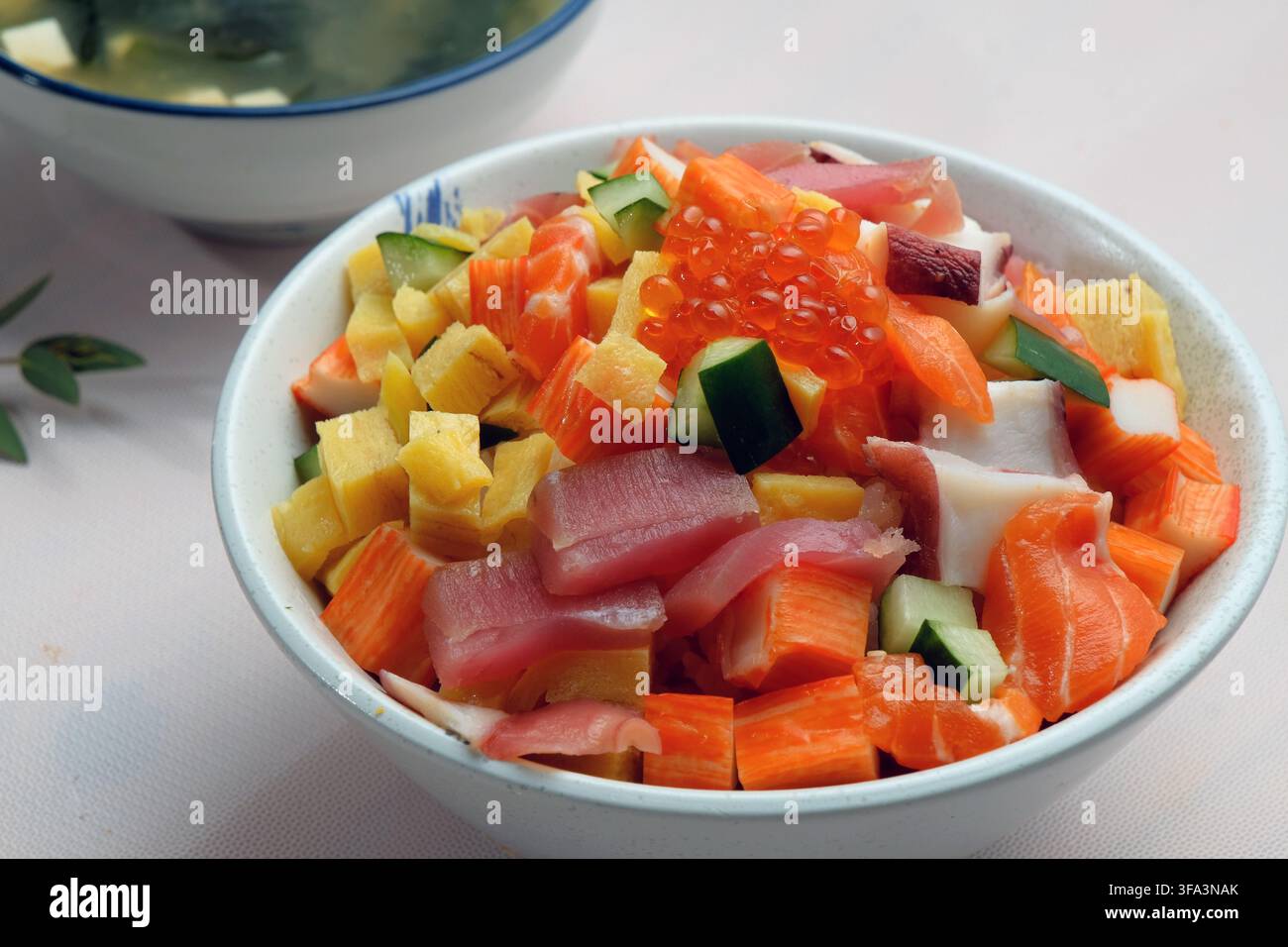 Una ciotola di pesci freschi tagliati a cubetti tra cui tonno, uova di salmone, bastoncini di granchio, ecc. che coprono il fiume giapponese chiamato chirashi don servito con miso s Foto Stock