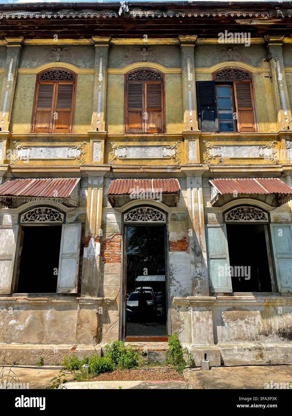 Una vista ad angolazione bassa di una vecchia facciata di edificio vintage con porte classiche in legno, finestre con persiane e dettagli invecchiati sotto un cielo azzurro Bangkok Thailandia - Immagine stock catturata con smartphone