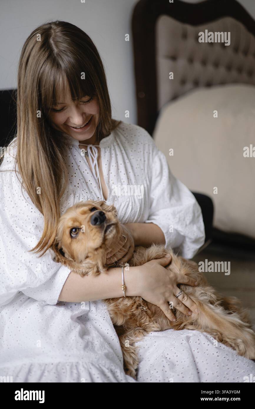 Donna in abito bianco che accarezza un cocker spaniel al chiuso, mostrando affetto e legame Foto Stock