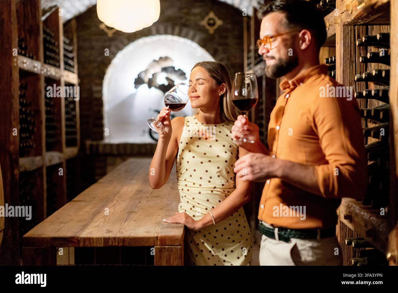 In una cantina calda e accogliente, una coppia assapora ricchi vini rossi condividendo sorrisi. La loro serata è colma di risate e sapori deliziosi. Foto Stock