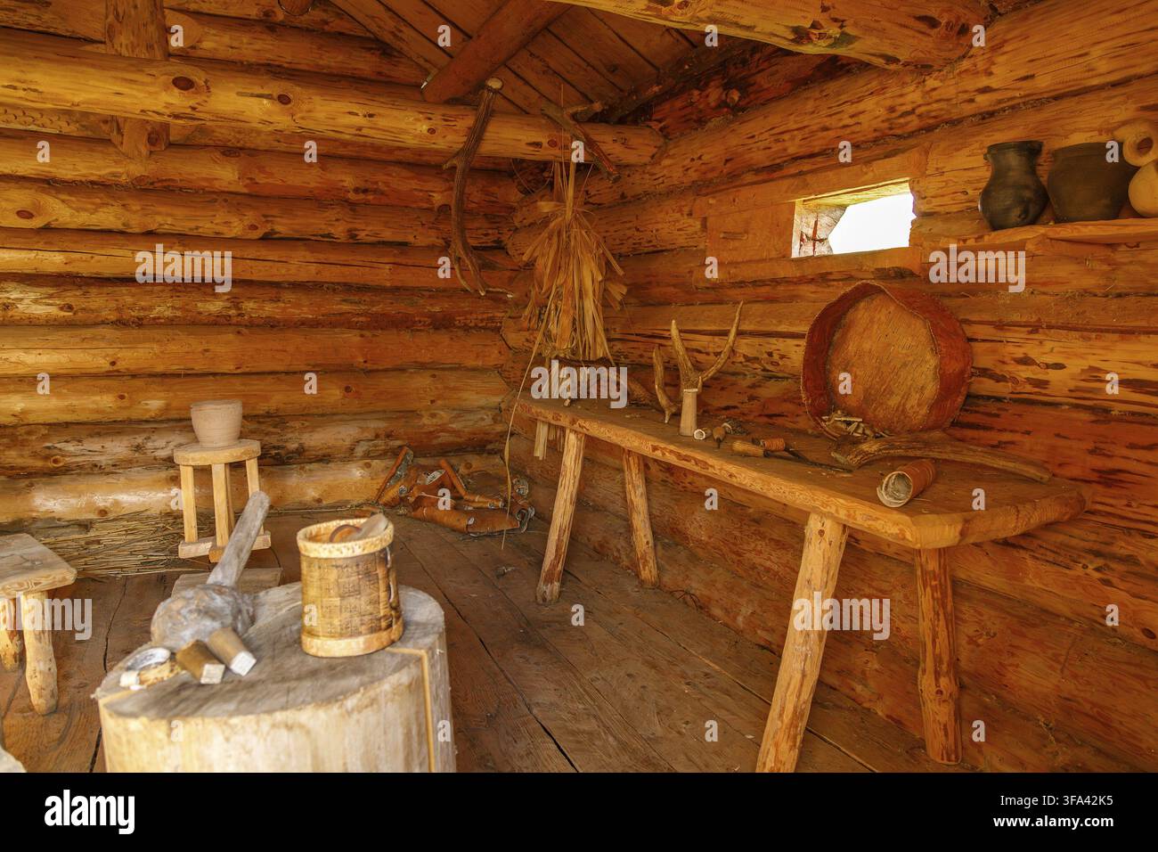 Interno di una capanna di legno rustica con strumenti artigianali, ceramiche in argilla e mobili tradizionali illuminati dalla luce naturale Foto Stock