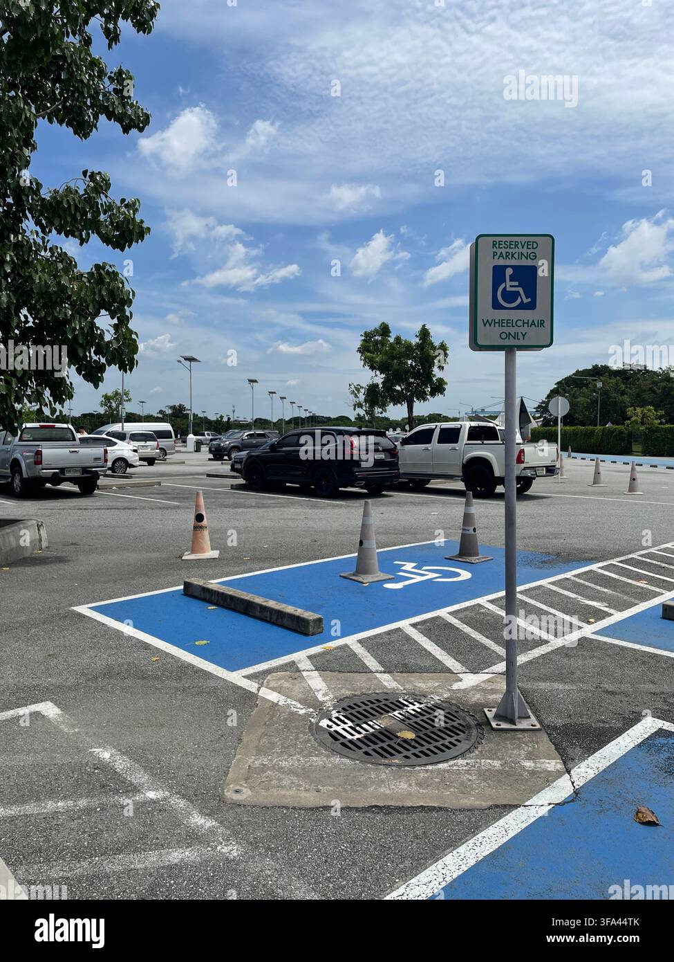 Un posto auto riservato agli utenti di sedia a rotelle, dipinto di blu con il simbolo internazionale di accessibilità, situato in un parcheggio all'aperto sotto un posto - Immagine stock catturata con smartphone
