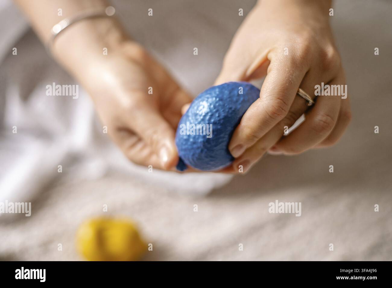 Mani concentrate nello spremere una palla sensoriale blu strutturata, evocando relax Foto Stock