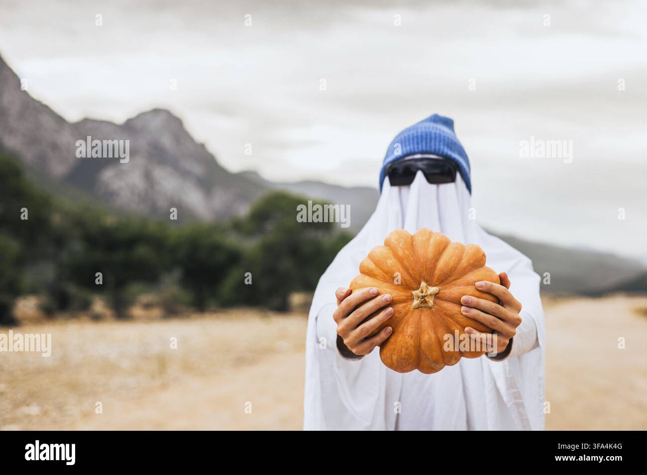 Fantasma di Halloween divertente che tiene una zucca all'aperto. Contenuto stagionale virale, idea di costume creativo e concetto di stile di vita autunnale moderno. Foto Stock