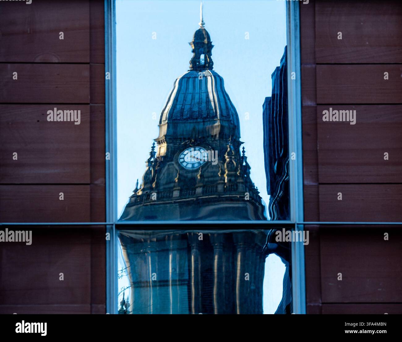 Riflessione della torre dell'orologio del Municipio di Leeds incorniciata in una finestra di vetro distorta di un edificio moderno Foto Stock