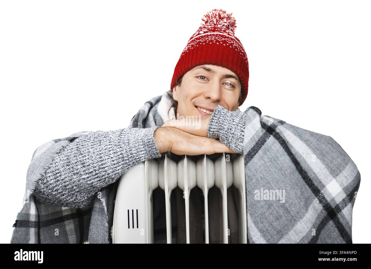 Giovane uomo felice con cappello invernale e coperta che si riscalda vicino a un riscaldatore elettrico. Su sfondo bianco Foto Stock