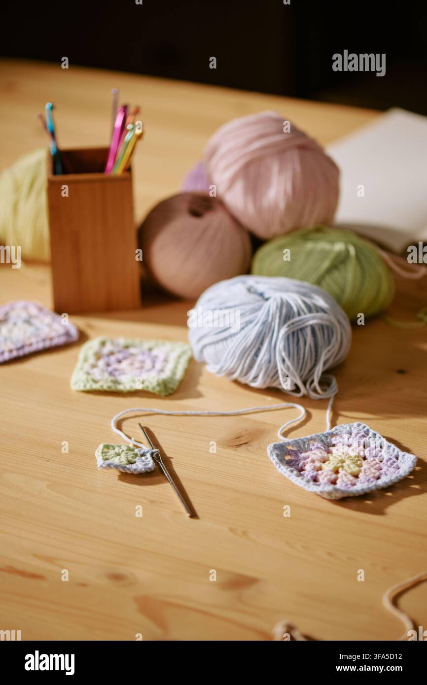 Palle di lana colorate e uncini per uncinetto sul tavolo in un laboratorio di maglia Foto Stock